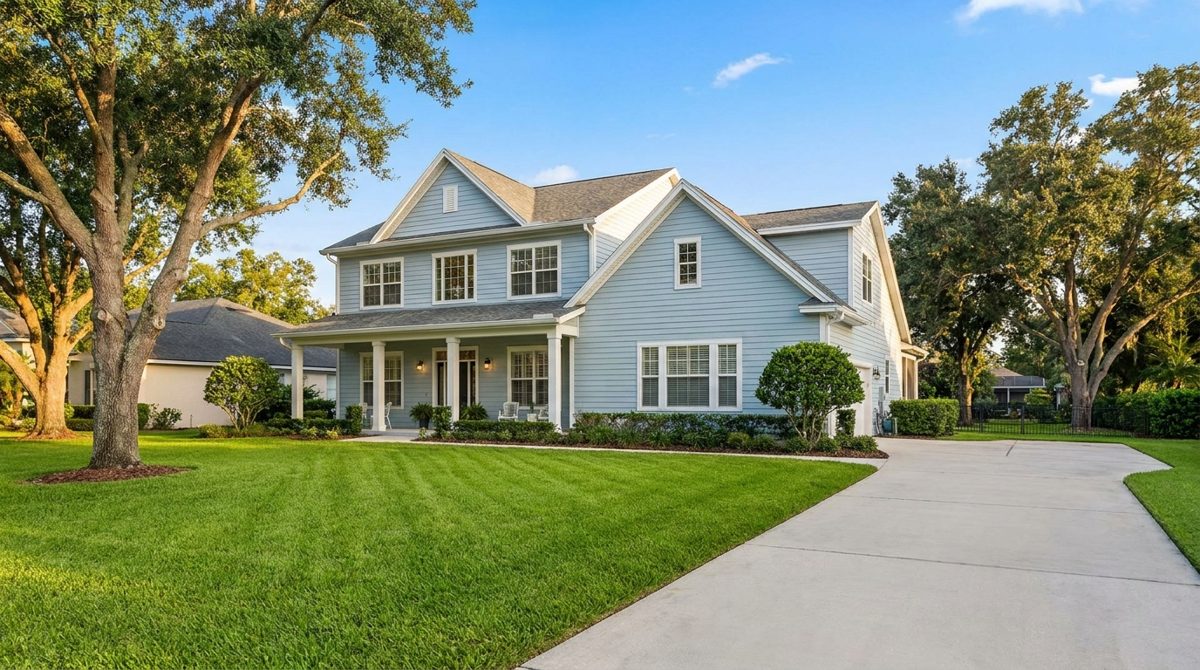 Bright two-story house with pale siding, white trim, a covered porch, a green lawn, and a clear blue sky